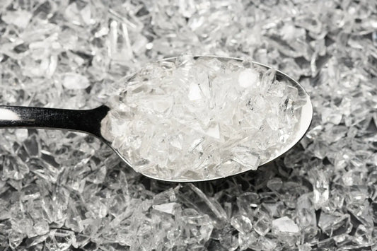 A spoonful of glass frit held over a pile of the same glass frit in an off white colour.