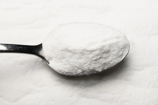 A close-up of a metal spoon filled with white powder, set against a textured white background.