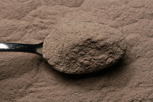 A metal spoonful of glass frit held over a pile of the same glass frit.