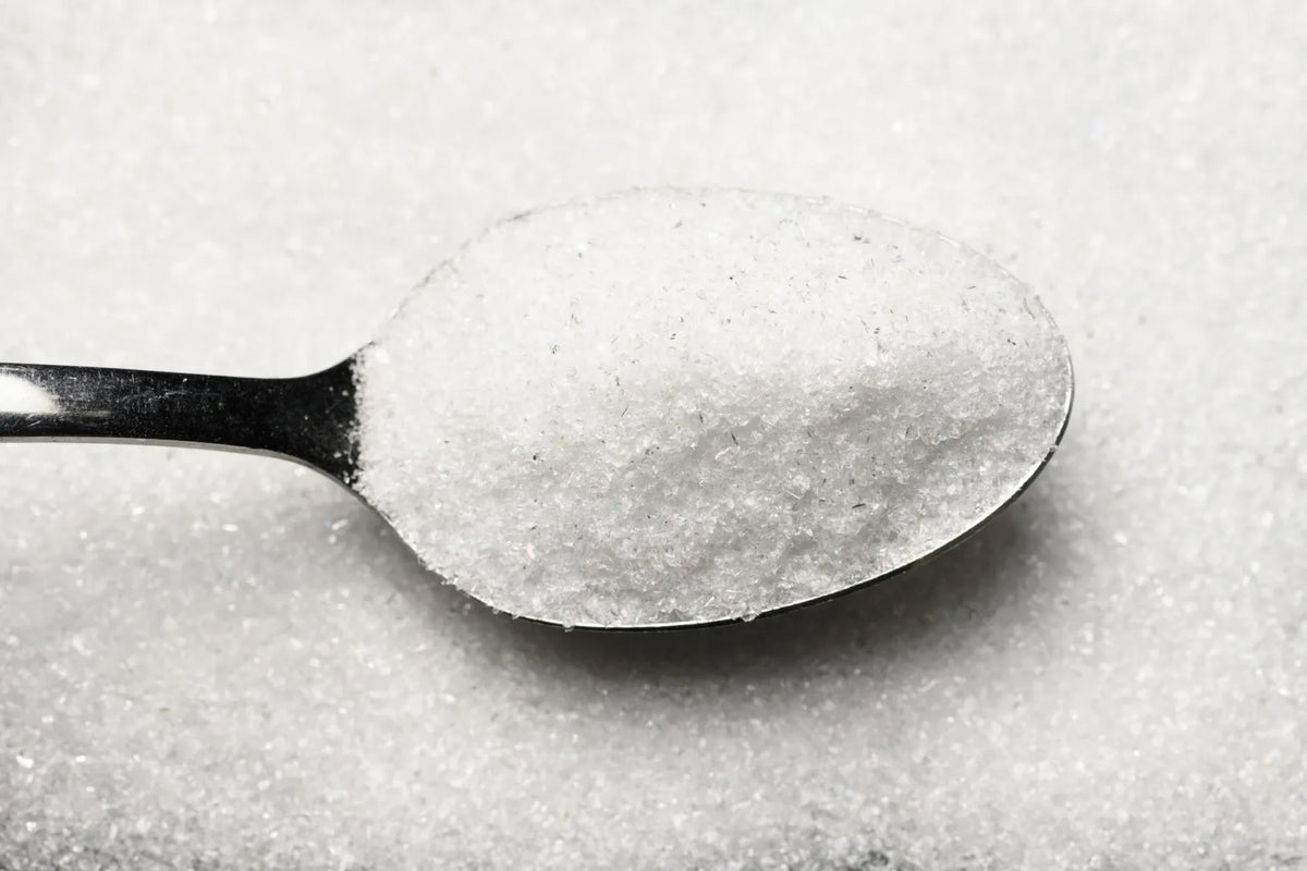 A spoonful of glass powder held over a pile of the same glass powder in a stark white colour.