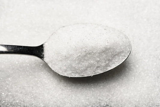 A spoonful of glass powder held over a pile of the same glass powder in a stark white colour.