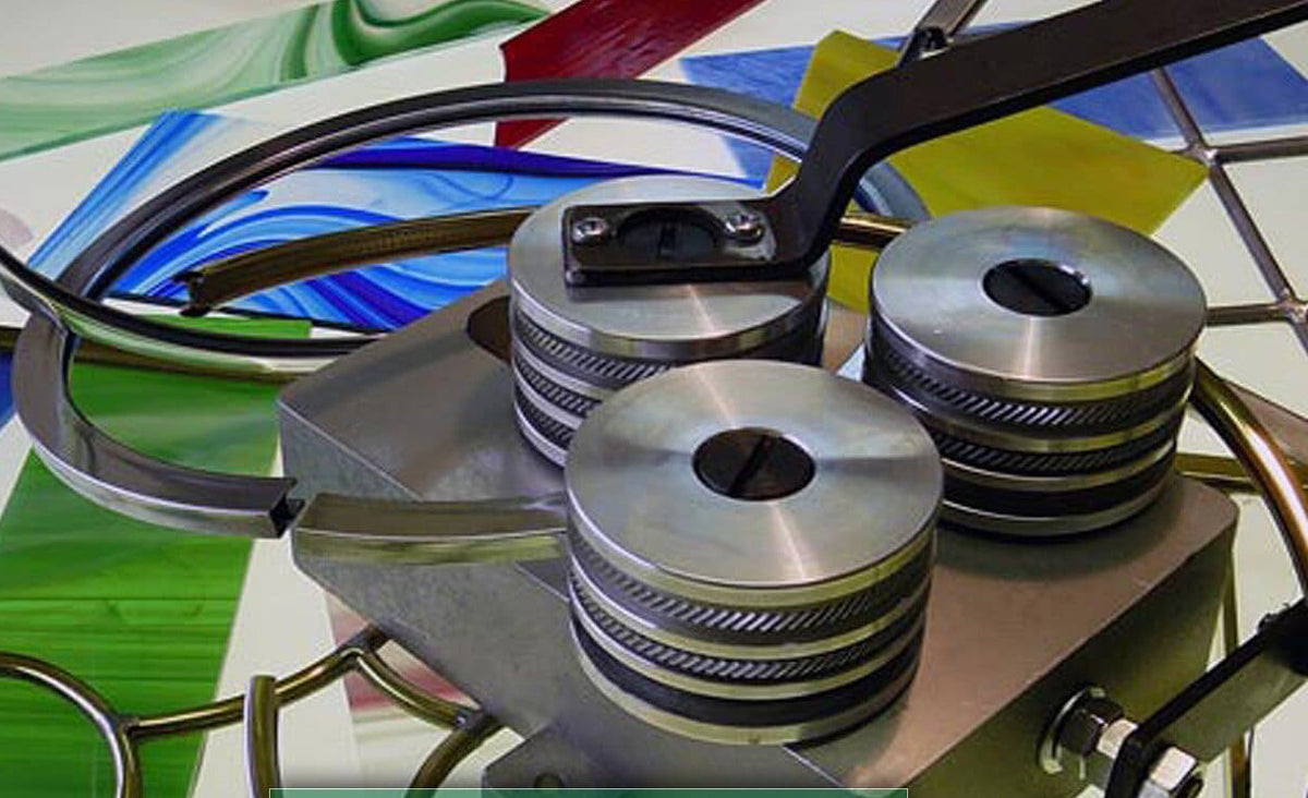 A close-up of a metallic press or stamping machine with three circular metal rollers and curved metal arms, set against a colorful abstract background.