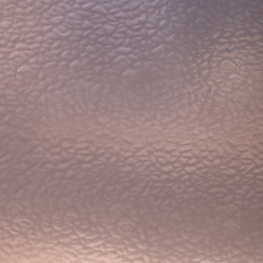 A close-up of a textured, hammered metallic surface with a warm copper or rose-gold tone.