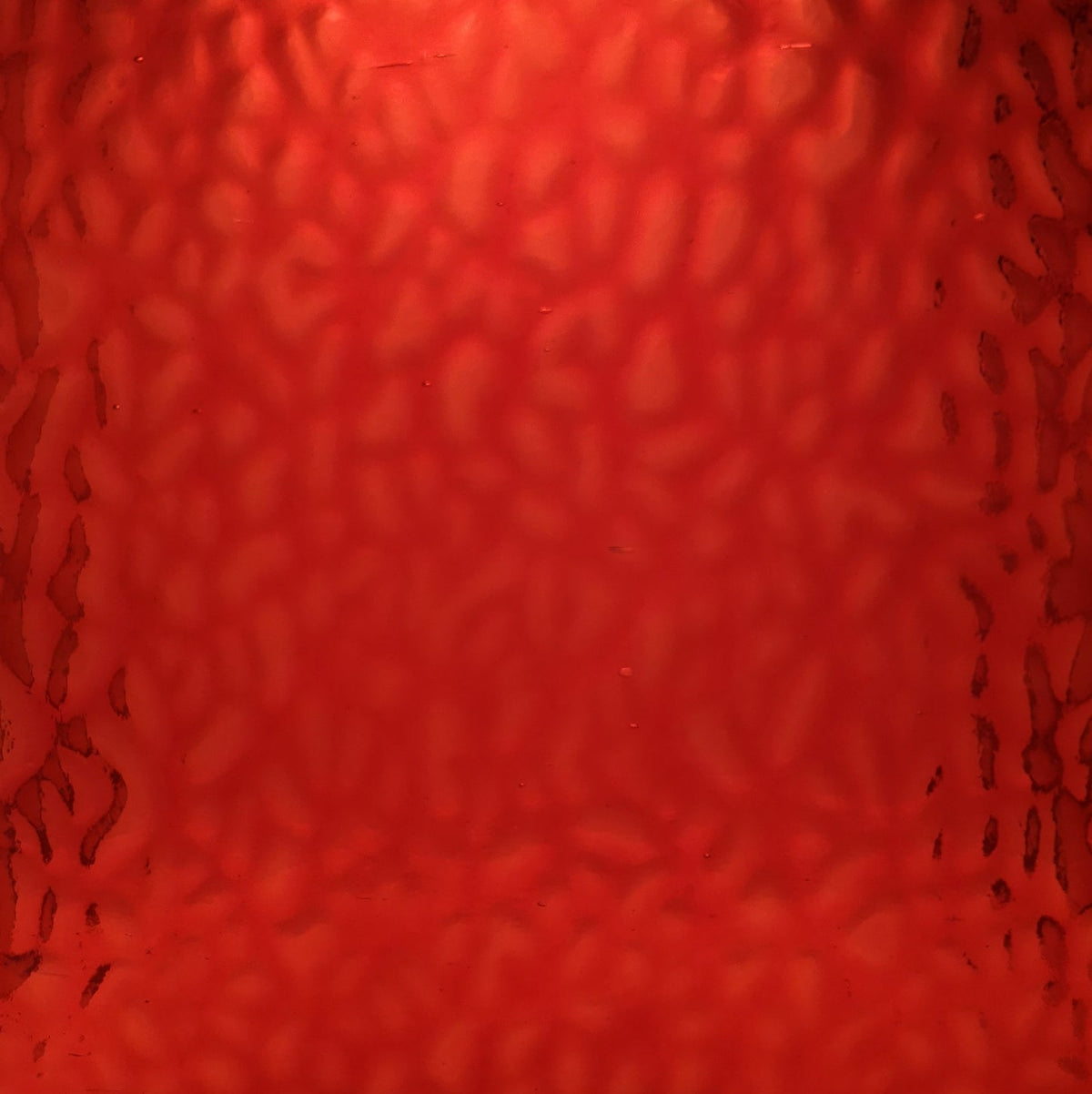 Red textured glass with a hammered or wavy pattern, filling the entire frame.